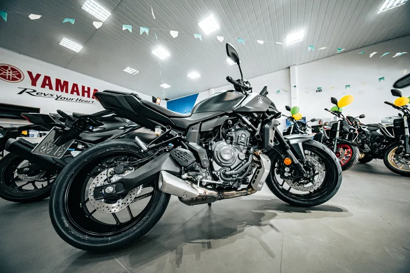 MT-07 cinza-escura vista de lado, com a parede Yamaha Revs Your Heart ao fundo.